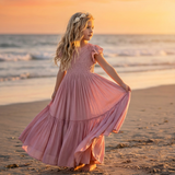 Young girl in a pink dress standing on a beach at sunset
