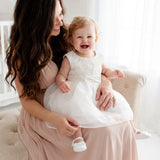 Woman holding a baby in a white dress in a bright room.